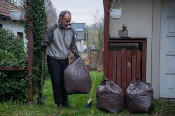 mężczyzna sprzątający opadłe liście do worków wokoło domu © siwyk
