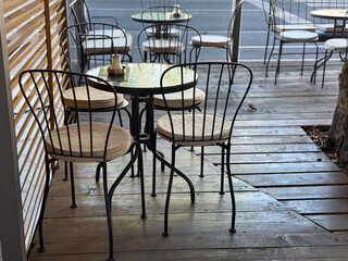 Outdoor cafe terrace with metal chairs and wooden floor. Calm morning atmosphere, urban lifestyle, and leisure moments in modern city setting.