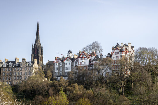 View of aged buildings with distinctive architectural styles nestle amongst budding trees under a serene sky, creating a timeless scene, Edinburgh, Scotland, United Kingdom.