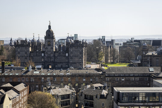 View of imposing grey stone architecture with intricate details and a clock tower rises above the city's skyline under a clear sky, Edinburgh, Scotland, United Kingdom.