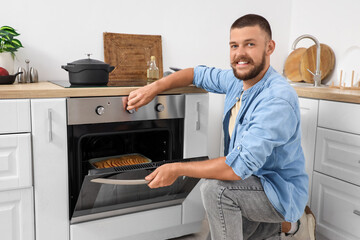 Young man adjusting electric oven with apple pie in kitchen