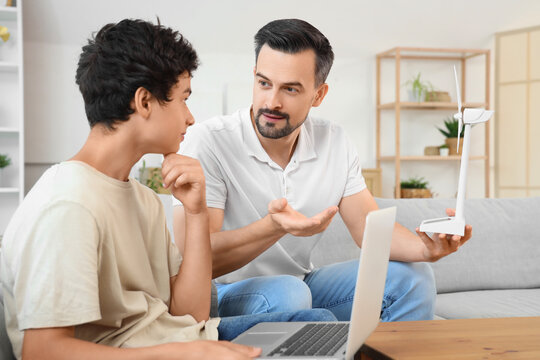 Teenage boy and his father with wind turbine model using laptop on sofa at home