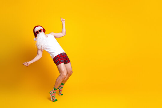 Playful santa claus in a white tank top and red plaid shorts dancing against a bright yellow background for a festive holiday image - Powered by Adobe