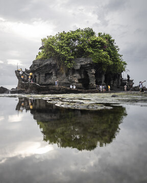 View of the majestic Tanah Lot temple perches dramatically on a rock formation, its reflection shimmering in the tranquil waters, Bali, Bali, Indonesia.