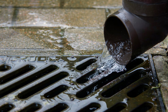 Rainwater drainage pipe flowing into metal grate outdoors