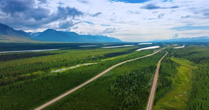 Roads and river in the beautiful vast valley among the mountains. Fluffy clouds cover the sky over the scenery. Alaska, USA. Aerial view.