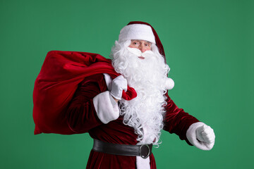 Santa Claus with red bag of Christmas gifts on green background