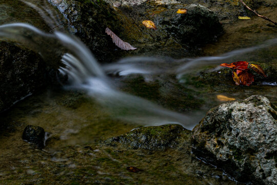 View of water cascading over mossy rocks, with scattered autumn leaves adding vibrant pops of color to the tranquil scene, Sharonville, Ohio, United States.