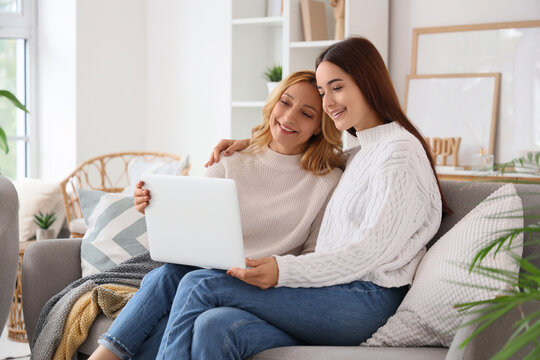 Pretty young woman with her mother video calling while sitting on sofa at home