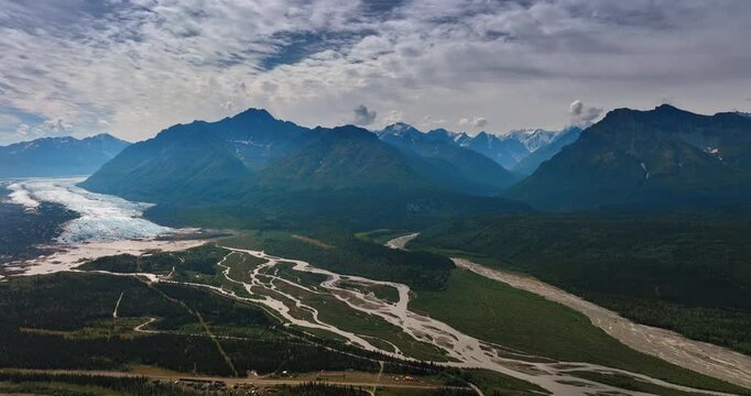 Glacier covers the park of the valley turning into branching river. Clouds cover the sky over the stunning rocks. Alaska, USA.