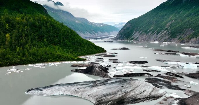 Footage over the river flowing among the rocks. Huge boulders of ice stick out from water. Clouds cover the tops of the mountains.