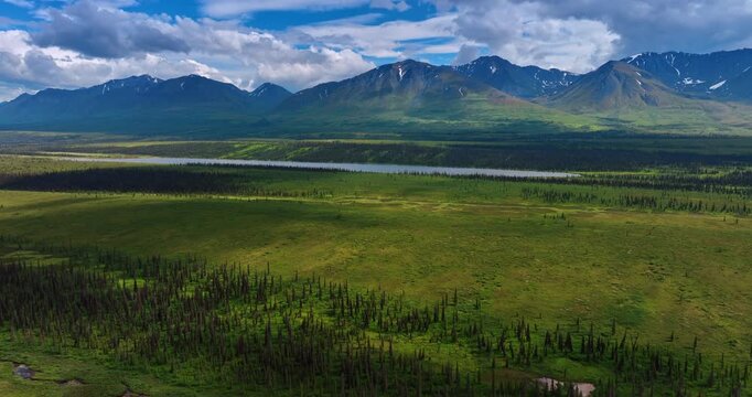 Rising over the vast green valley with long pond. Striking mountains and beautiful clouds above them at backdrop.