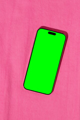 Smartphone with a green chroma key screen lying on bright pink denim fabric.