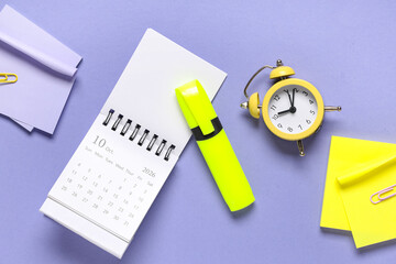 Calendar with alarm clock and stationery on purple background