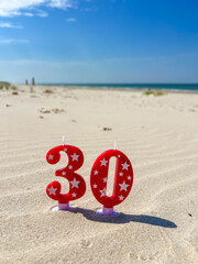 Leba, Poland, July 19, 2025, Red foil number 30 birthday celebration balloons standing on sandy Baltic Sea beach in Leba Poland summer day. High quality photograph