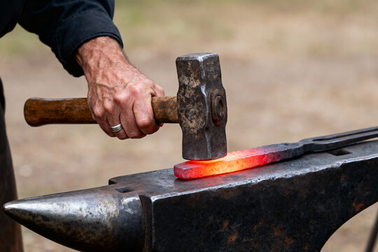 Blacksmith hammering glowing hot metal on an anvil in a workshop