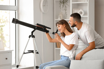 Young couple looking through telescope at home