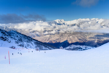 Skiers on a slope descending from a mountain, with a stunning view of snow-capped mountains