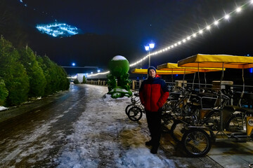 A night shot of a man standing next to walking bicycles, against the background of mountains.