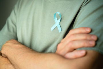 Man standing with crossed arms wearing blue satin ribbon on shirt. Concept of prostate cancer awareness in November, prevention, early diagnosis, and medical care for mens health.