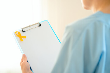 Close up of female doctor and nurse in medical uniform holding clipboard with yellow ribbon and empty sheet. Symbol of childhood cancer awareness, medical support, diagnosis, and family care.