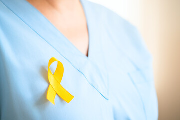 Close up of healthcare professional woman in uniform with yellow ribbon. Represents support for children with cancer, medical care, timely diagnosis, family assistance, and health awareness.