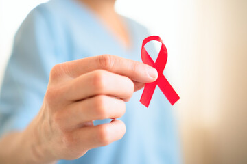 Extreme close up of female hand holding red satin awareness ribbon, symbolizing HIV AIDS solidarity, support and hope for future treatment.