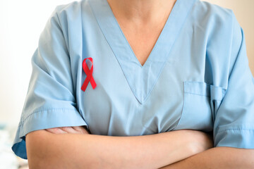 Female medical professional with crossed arms showing red awareness ribbon on uniform, demonstrating HIV AIDS solidarity and determined support.