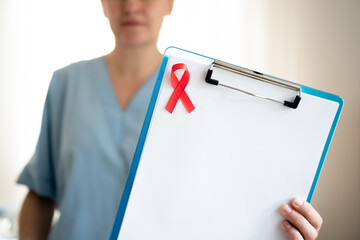 Friendly medical professional with red AIDS awareness ribbon holding medical forms, showing compassionate care for HIV patients and community.