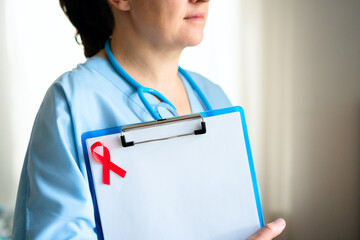 Kind female doctor with stethoscope around neck and red awareness ribbon on uniform, smiling warmly for HIV patient support and care.