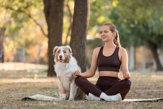 Sporty young woman with Australian Shepherd dog meditating in park - Powered by Adobe