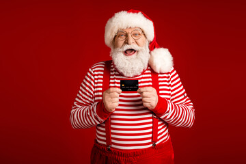 Cheerful Santa with credit card wearing red striped shirt suspenders and hat smiles at camera ready for Christmas holiday promotion