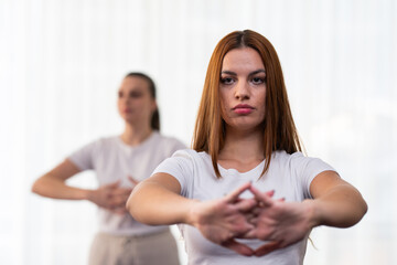 Focused young woman in a white shirt performing a stretching exercise indoors. Concept of wellness, health, flexibility, mindfulness, and active lifestyle.
