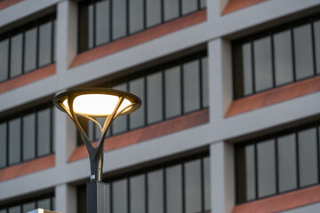 Modern LED streetlight illuminated in front of a contemporary office building facade, representing urban infrastructure, sustainable lighting technology, and energy-efficient city design.