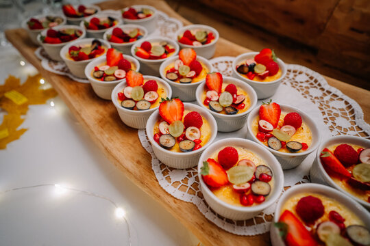 Delicious dessert cups filled with creamy custard topped with fresh strawberries, raspberries, and grapes arranged beautifully on a wooden serving board with lace doily