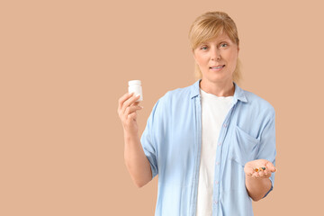 Mature woman with vitamin supplements on beige background
