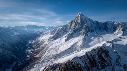 Spectacular aerial view of majestic snow-covered jagged mountain peaks with sharp ridges, steep slopes, and dramatic rocky formations under bright blue sky with clouds, alpine scenery.