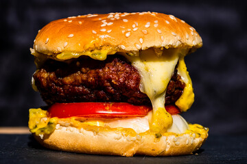 Detail of fresh tasty beef cheeseburger with melted cheese isolated on black background
