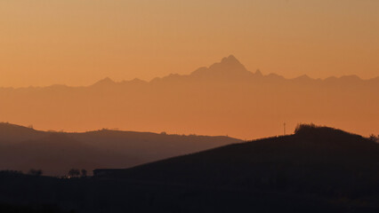 Stunning evening sunset over Piedmont's Langhe and Asti region, with the majestic snow-capped Monte Rosa and Alps glowing in warm alpenglow against a dramatic pink-orange sky. Perfect panoramic vista 