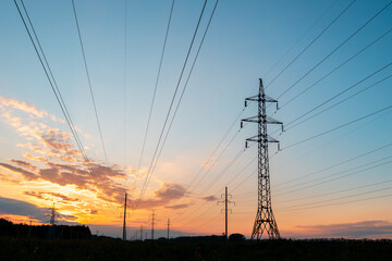 A tall power tower with many wires is silhouetted against a beautiful sunset sky