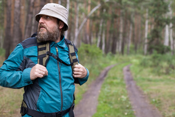 A man with a beard in a panama hat is wearing a backpack on his back