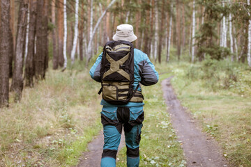 A man in a backpack and hat walks along a dirt road in the forest