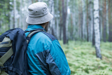 A man wearing a hat and a blue jacket is walking through a forest