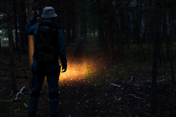 A man with a panama hat is walking along a path and shining a flashlight in front of him