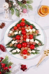 Traditional holiday salad in the form of a live edible Christmas tree with feta cheese, olives, tomatoes and grapes, Christmas and New Year's dishes, food design idea, fir branches and decorations