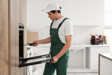 Male worker with screwdriver installing built-in oven in kitchen