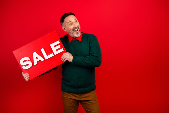 Funny shopper man holds bold sale sign in red studio and looks amused by big discount
