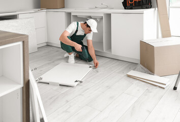 Male worker with drill assembling furniture in kitchen