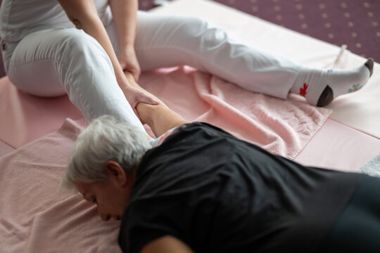 A physiotherapist assisting an older woman with a shoulder and arm stretch while lying on a mat. Rehabilitation and physiotherapy session concept focusing on mobility, flexibility, pain relief, and