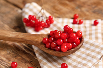 Spoon with fresh viburnum berries on wooden background, closeup